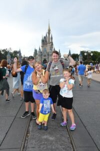 Lauren hersey at Disney World with family in Magic Kingdom wearing Disney outsides posing in front of the castle 